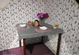 Na zdjęciu znajduje się dziewczynka z głową na talerzu w magicznym stole.