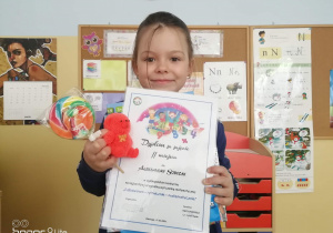 Na zdjęciu znajduje się dziewczynka z dyplomem i nagrodami.