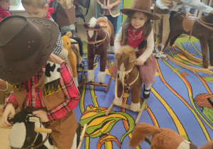 Na zdjęciu znajdują się dzieci bawiące się na koniach na biegunach.