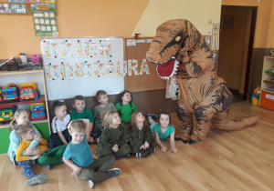 Na zdjęciu znajdują się dzieci z grupy Motylków oraz dinozaur, w tle widać napis dzień dinozaura